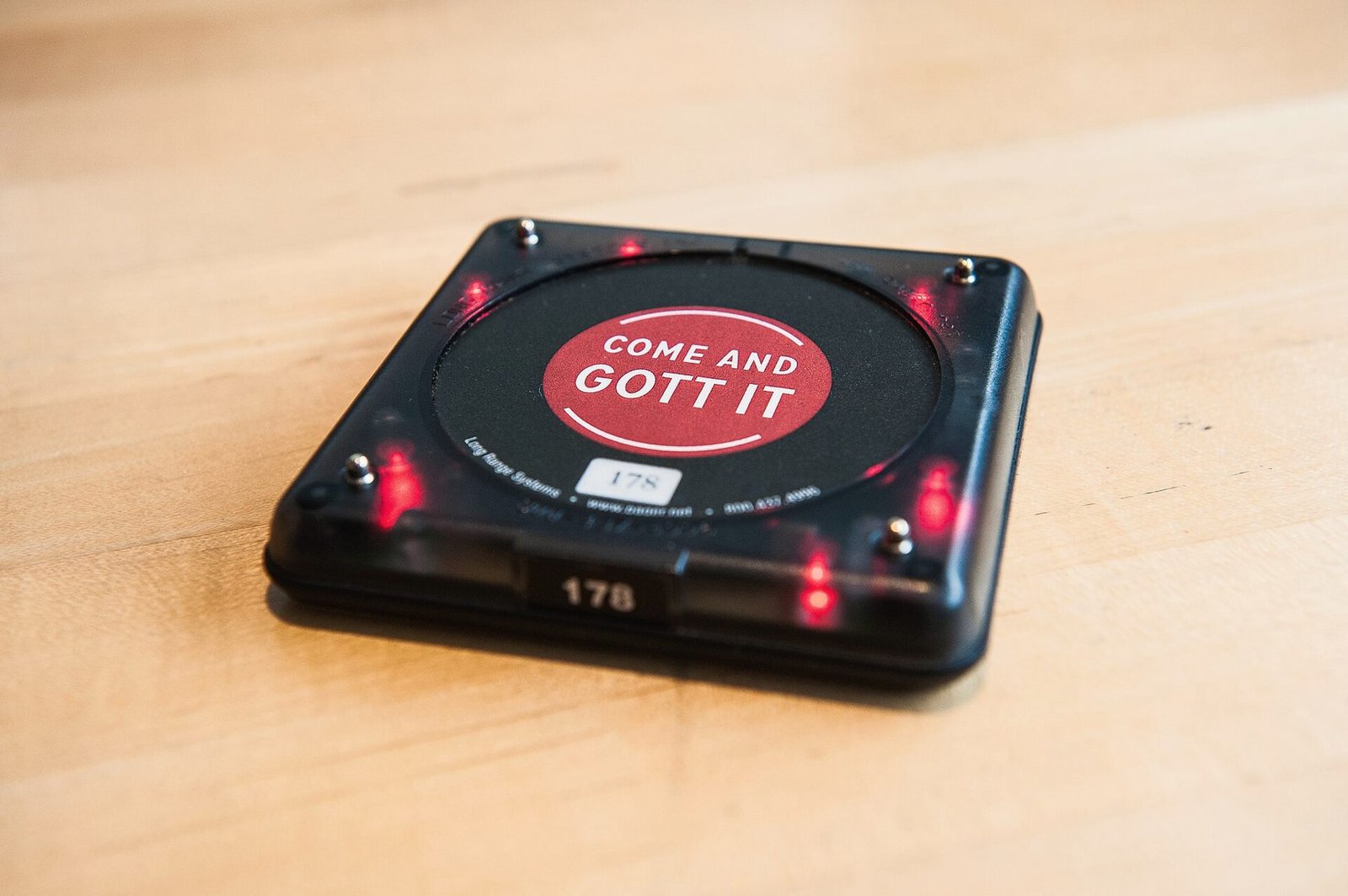 A flat coaster-style pager with lights around its edge resting on a table.